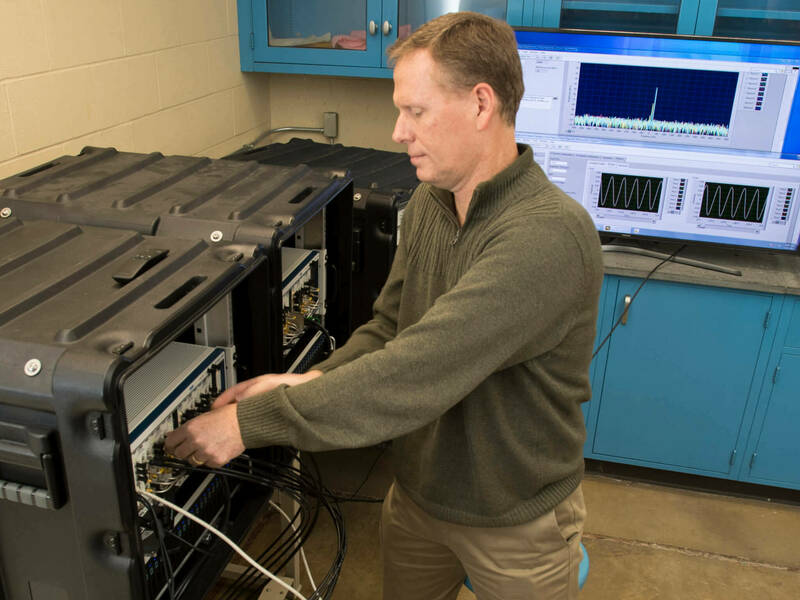 Robert Kossler in the RF Communications and Sensing Lab standing in front of and working on radio equipment