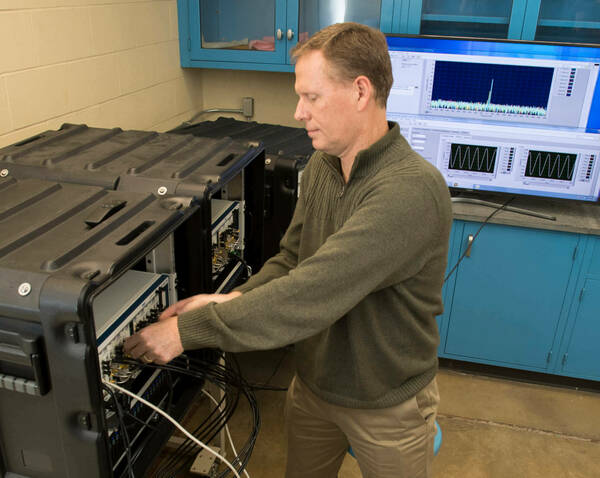 Robert Kossler in the RF Communications and Sensing Lab standing in front of and working on radio equipment