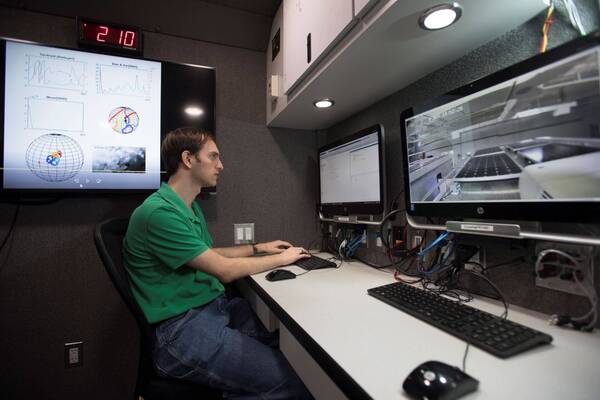 inside field research vehicle with Eric Jesse at workstation in front of a monitor. An additional workstation is seen in the foreground